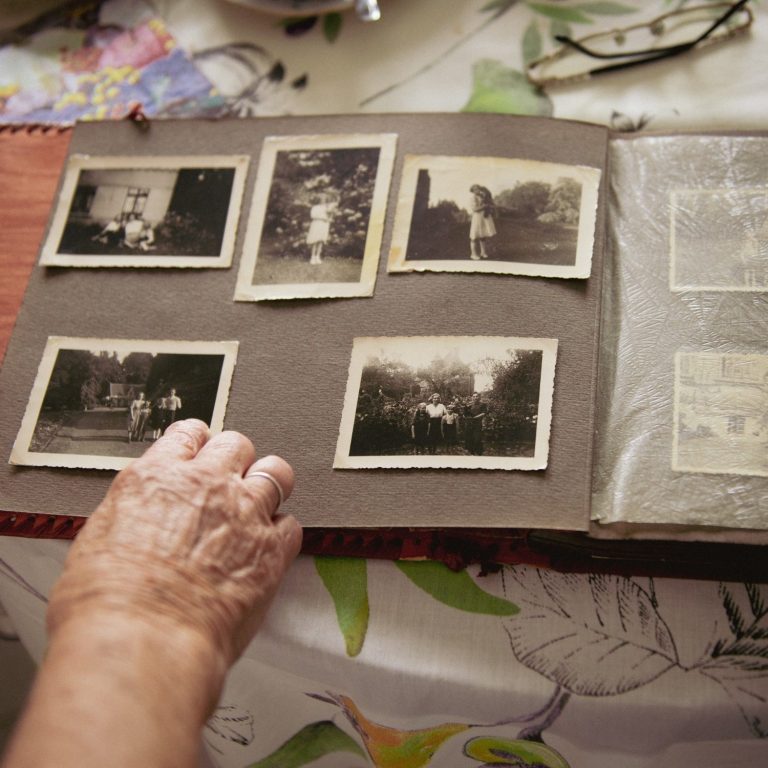 Une main feuilletant un album de photos anciennes sur une table. Photographies de famille